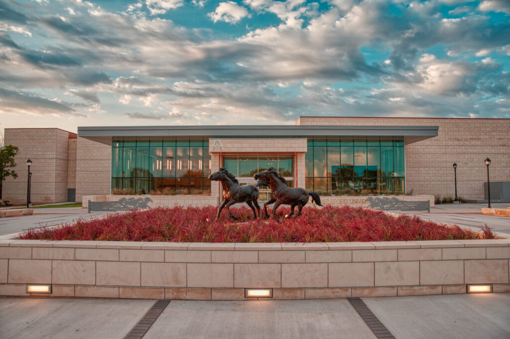 The glass entrance of the UTA University Center featuring a bronze horse statue out front.