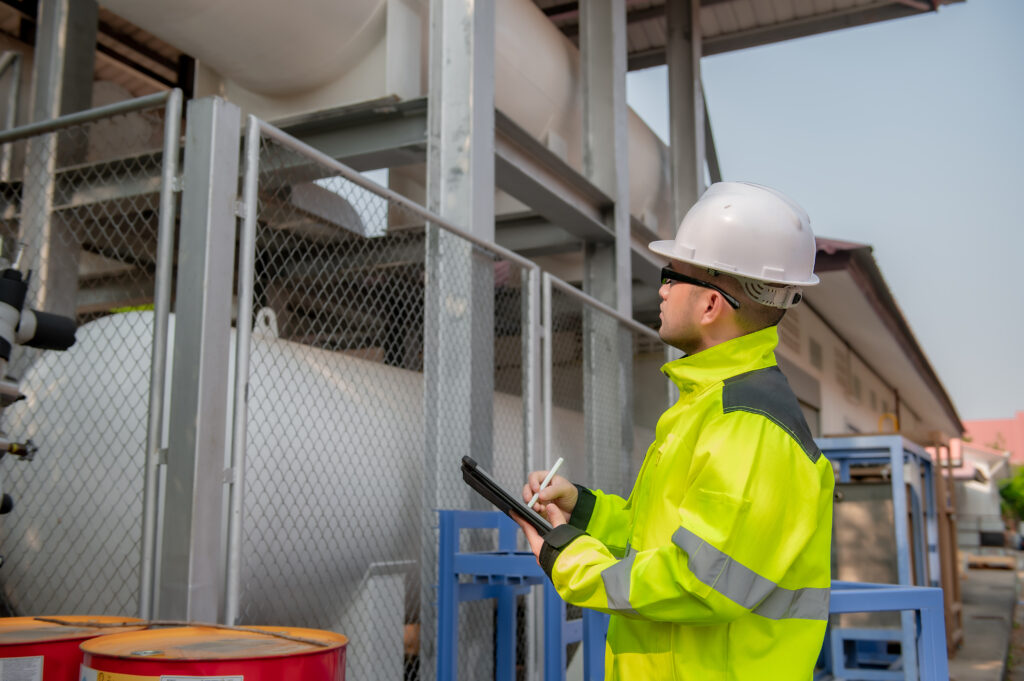 A worker in a high-visibility jacket and hard hat performing an industrial site inspection.