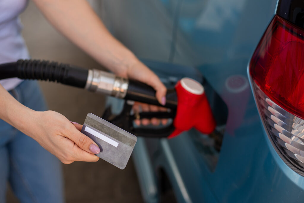 Close-up of a person holding a payment card while refueling a blue vehicle.