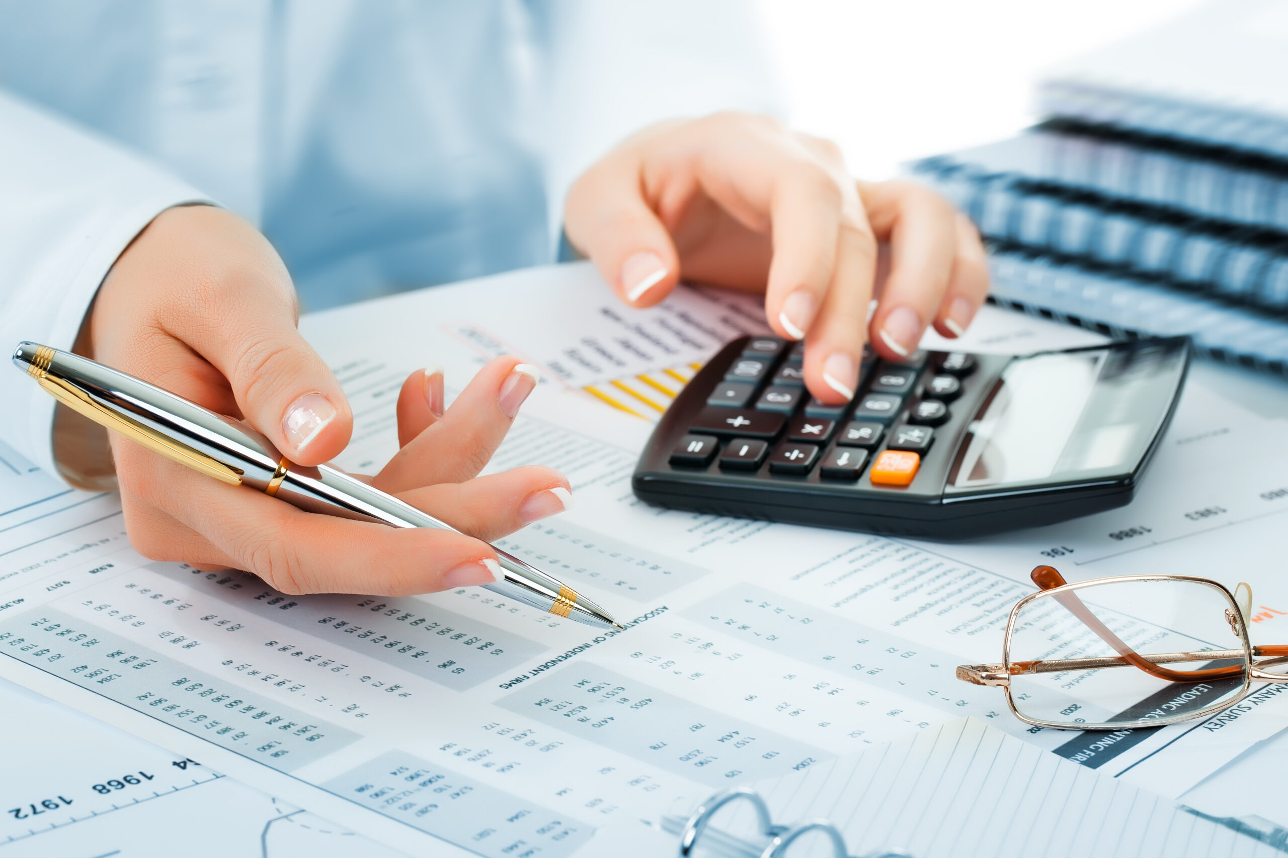 Close-up of hands using a calculator and pen to review financial spreadsheets.