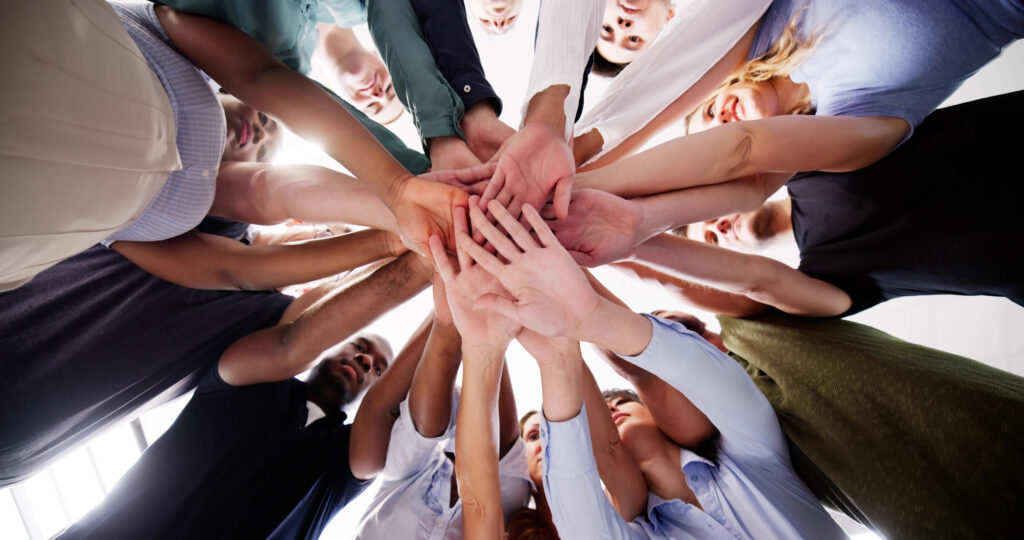 Low-angle view of a diverse group of people placing their hands together in a circle.