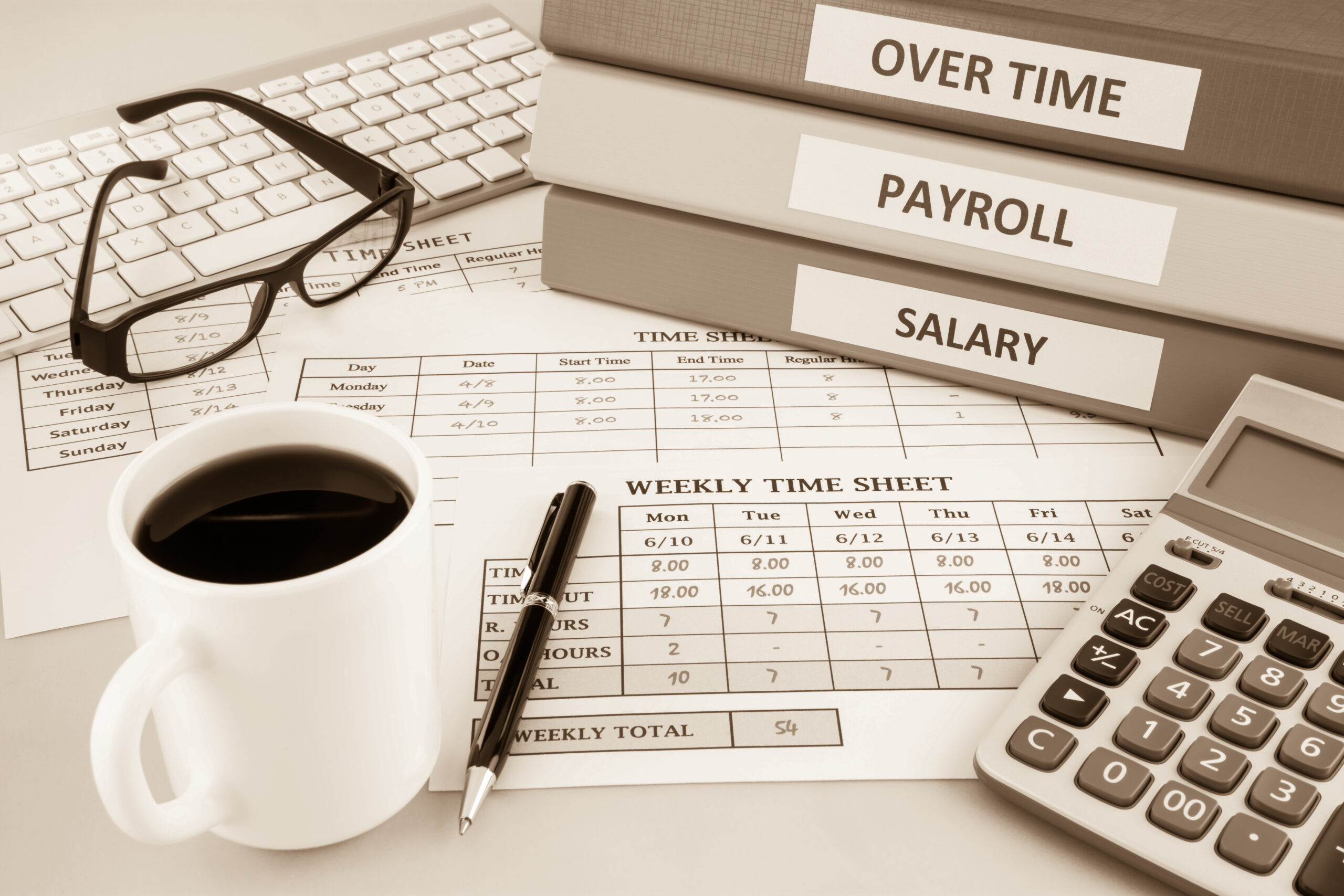 Desk arrangement with a calculator, coffee mug, and binders labeled Salary and Payroll.