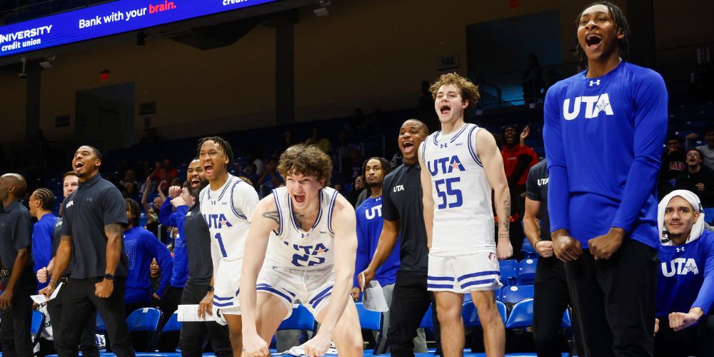 The UTA Mavericks men's basketball team cheering enthusiastically from the sidelines during a game.